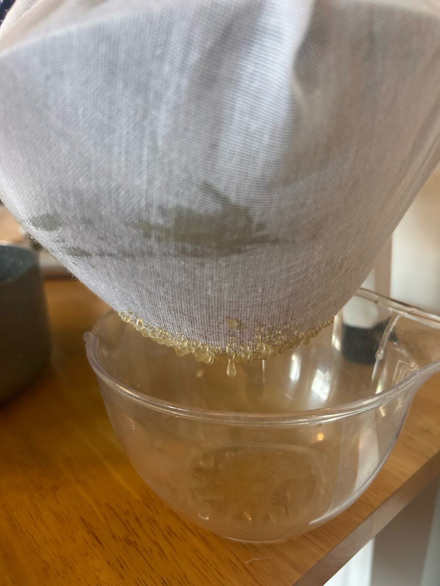 The first light, crystal-clear honey beading through muslin into a glass bowl