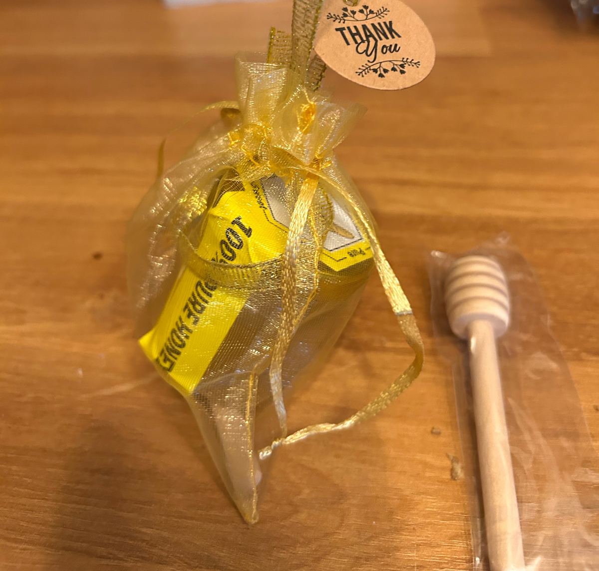 A jar of this batch in a gold organza bag, with a thank-you tag and a wooden honey dipper